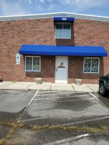 The front entrance of L&D Shop Equipment with a long blue awning hanging over the door two windows (one on either side) and a smaller blue awning over a window that is centered over the door. The awning has a unit number: 188.